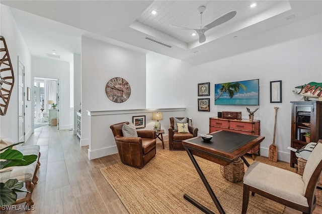 office area featuring ceiling fan, light hardwood / wood-style floors, and a tray ceiling