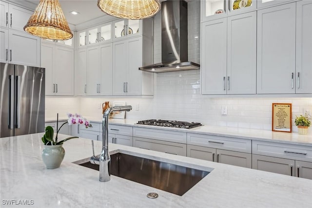 kitchen featuring light stone countertops, appliances with stainless steel finishes, wall chimney range hood, sink, and backsplash