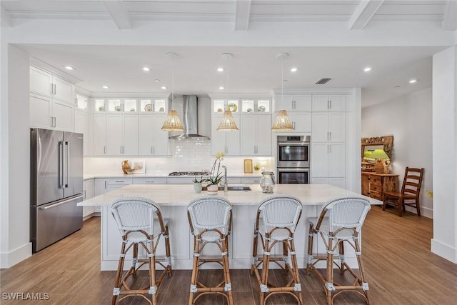 kitchen with wall chimney range hood, white cabinets, appliances with stainless steel finishes, and a spacious island