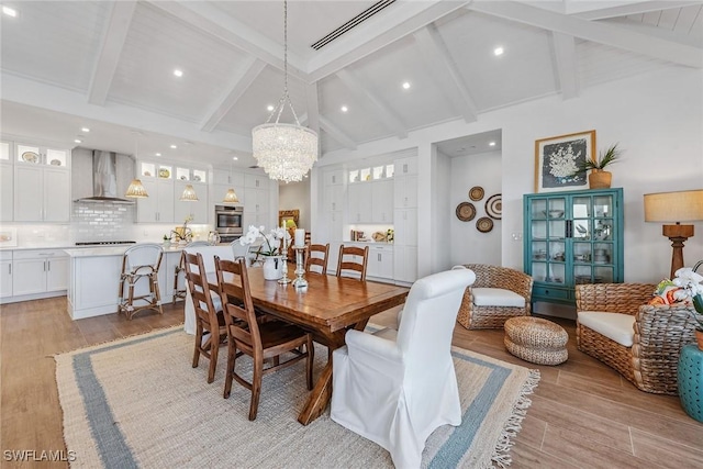 dining area with light hardwood / wood-style flooring, an inviting chandelier, and lofted ceiling with beams