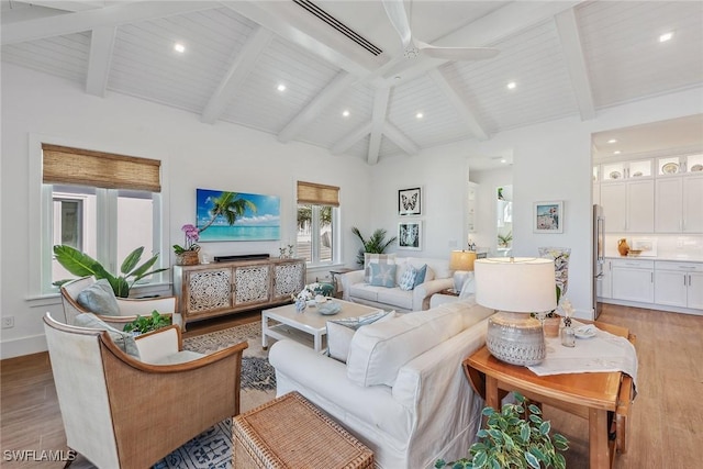 living room featuring light wood-type flooring, ceiling fan, beam ceiling, and a towering ceiling