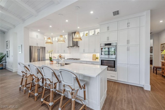 kitchen featuring wall chimney exhaust hood, stainless steel appliances, sink, a kitchen island with sink, and beam ceiling