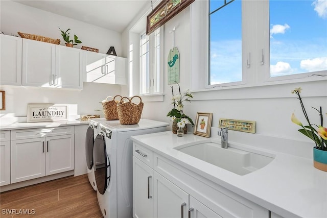 clothes washing area with sink, wood-type flooring, cabinets, and washer and dryer