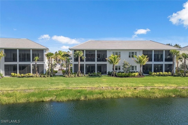 rear view of property featuring a sunroom, a water view, and a lawn