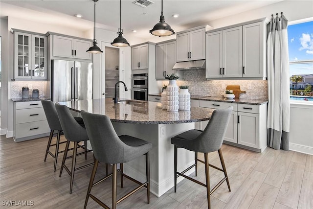 kitchen featuring decorative light fixtures, sink, stainless steel appliances, and an island with sink