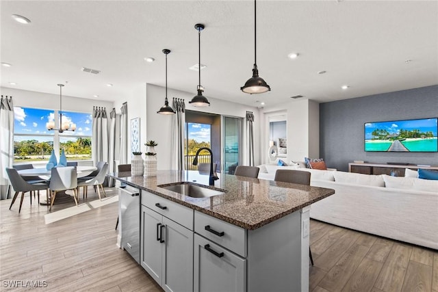 kitchen featuring a kitchen island with sink, dark stone counters, sink, and pendant lighting