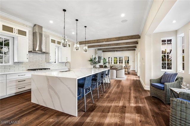 kitchen with white cabinetry, a large island, wall chimney range hood, beam ceiling, and light stone counters