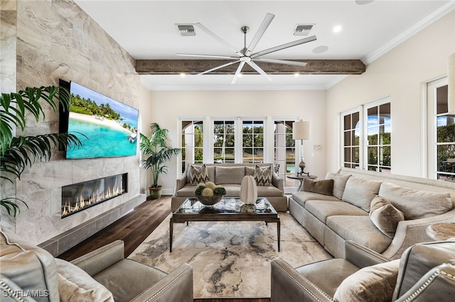 living room featuring a wealth of natural light, wood-type flooring, a tile fireplace, and beam ceiling