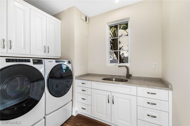 clothes washing area with sink, washing machine and clothes dryer, dark hardwood / wood-style flooring, and cabinets