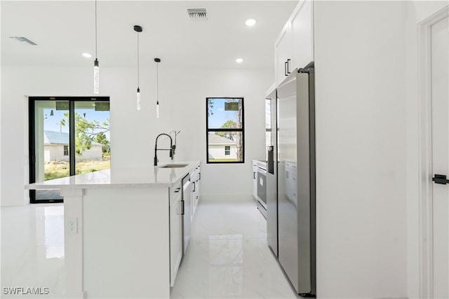 kitchen with white cabinetry, an island with sink, sink, stainless steel fridge, and hanging light fixtures