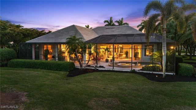 back house at dusk with a yard, a patio area, and glass enclosure