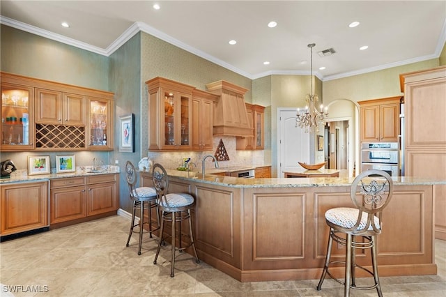 kitchen featuring custom range hood, decorative light fixtures, light stone countertops, and a breakfast bar area