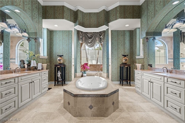 bathroom featuring decorative columns, ornamental molding, tiled tub, and vanity