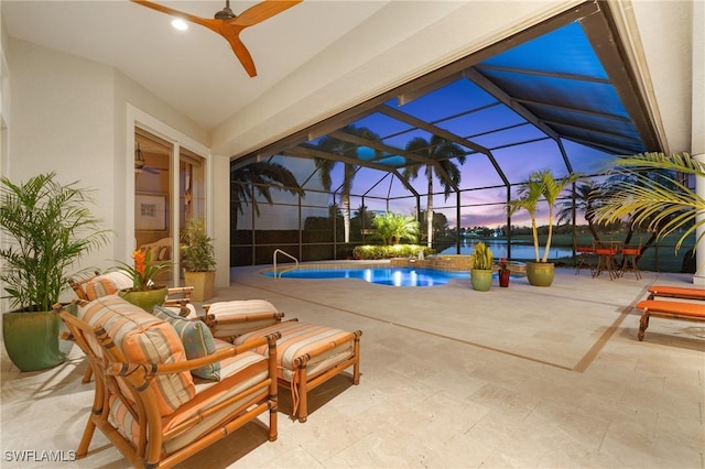 pool at dusk featuring a water view, a patio area, ceiling fan, and a lanai