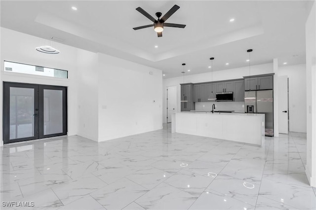 unfurnished living room with ceiling fan, sink, a raised ceiling, and french doors