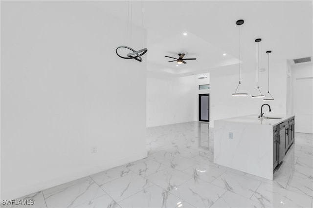 kitchen with pendant lighting, sink, ceiling fan, light stone counters, and a tray ceiling