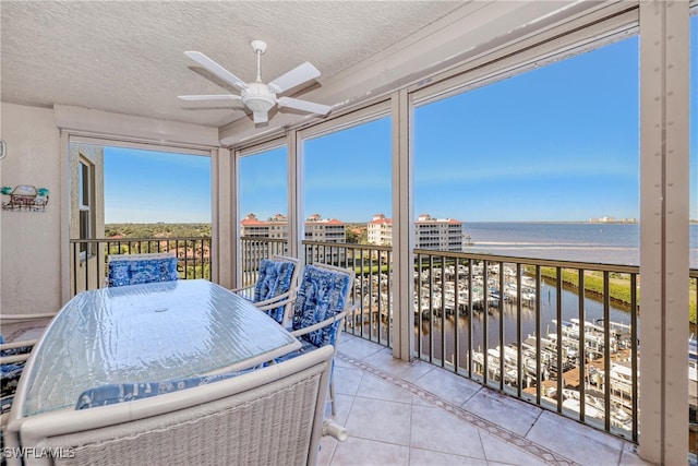 sunroom featuring a water view, ceiling fan, and a beach view