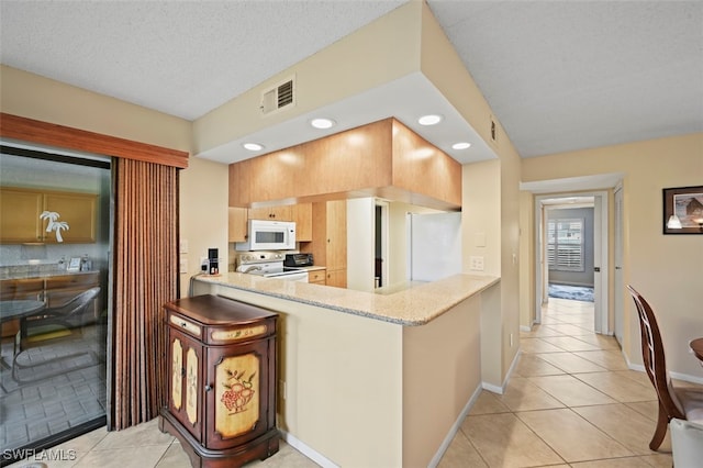 kitchen with white appliances, a textured ceiling, light tile patterned floors, kitchen peninsula, and light brown cabinets