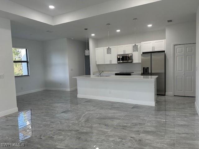 kitchen with appliances with stainless steel finishes, pendant lighting, a kitchen island with sink, and white cabinets