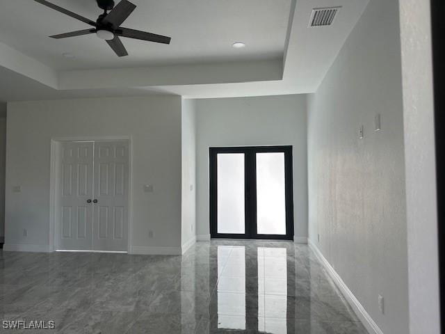 interior space with a tray ceiling, ceiling fan, and french doors