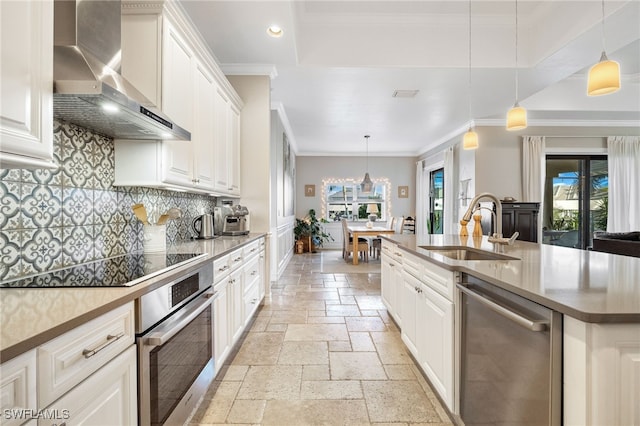 kitchen featuring sink, white cabinetry, decorative light fixtures, appliances with stainless steel finishes, and wall chimney range hood