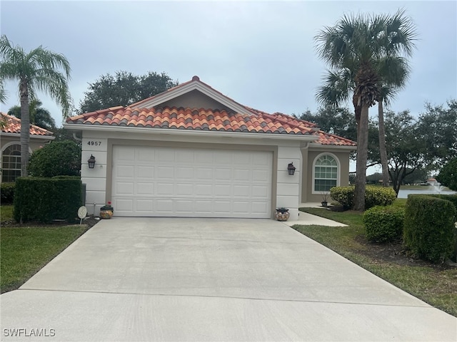 mediterranean / spanish house with a tile roof, stucco siding, an attached garage, and concrete driveway