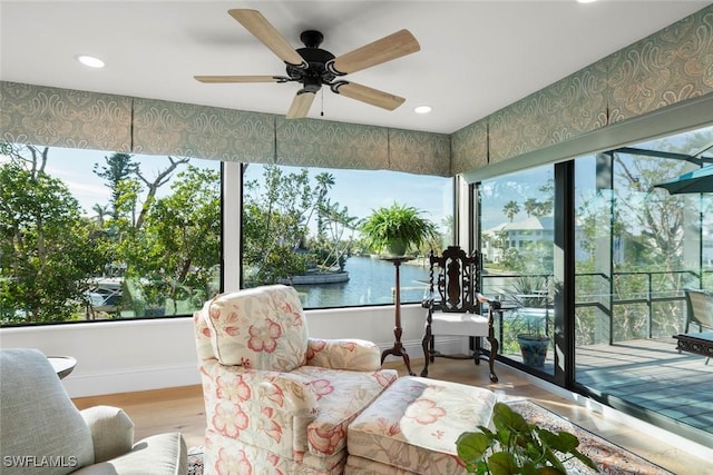 sunroom with a ceiling fan and a water view