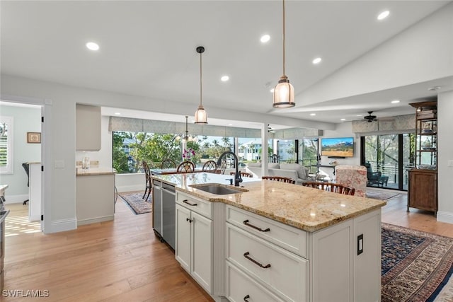 kitchen with a kitchen island with sink, a sink, white cabinets, open floor plan, and light stone countertops