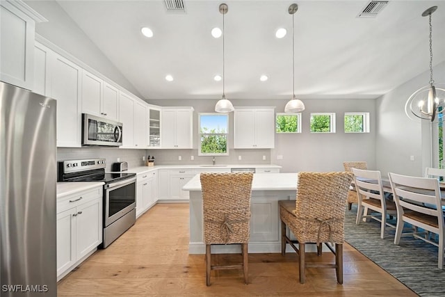 kitchen featuring appliances with stainless steel finishes, white cabinetry, backsplash, hanging light fixtures, and light wood-type flooring