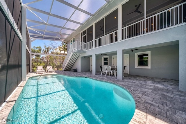 view of swimming pool with ceiling fan, a patio area, and glass enclosure