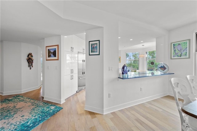 kitchen featuring white cabinets, hanging light fixtures, kitchen peninsula, and light hardwood / wood-style floors