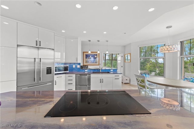 kitchen with pendant lighting, appliances with stainless steel finishes, backsplash, white cabinetry, and a wealth of natural light