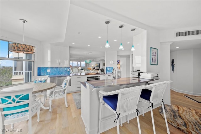 kitchen with kitchen peninsula, a kitchen breakfast bar, hanging light fixtures, white cabinets, and tasteful backsplash