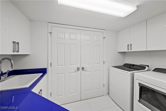 washroom with sink, washing machine and clothes dryer, light tile patterned floors, and cabinets