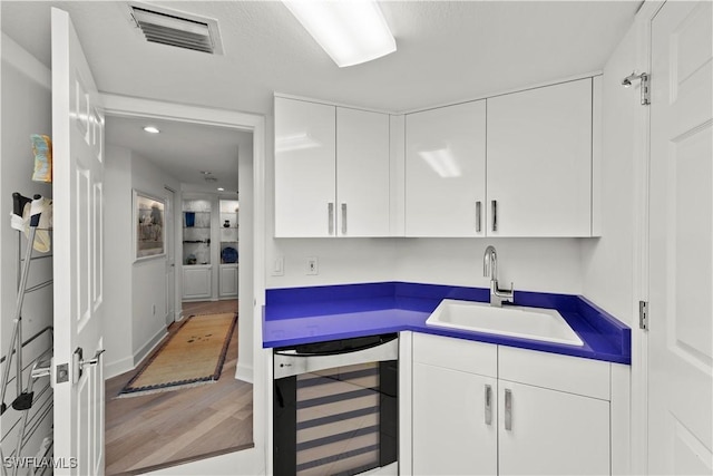 kitchen with white cabinets, wood-type flooring, beverage cooler, and sink