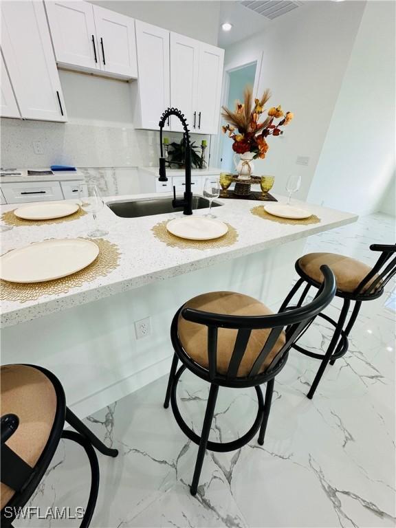 kitchen with white cabinetry, light stone countertops, sink, and decorative backsplash