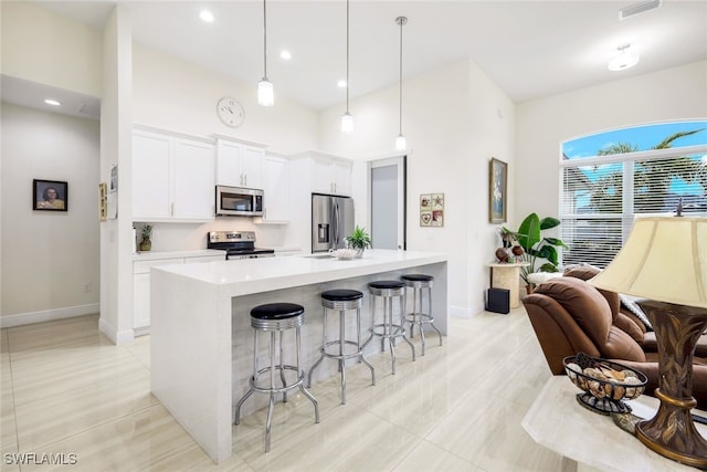 kitchen with stainless steel appliances, an island with sink, white cabinets, a kitchen bar, and decorative light fixtures