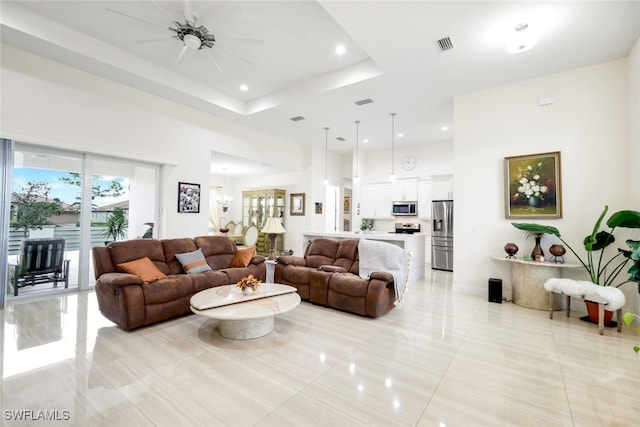 living room with ceiling fan, a tray ceiling, light tile patterned floors, and a high ceiling