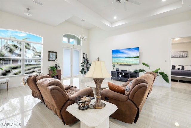 tiled living room with ceiling fan with notable chandelier, french doors, and a raised ceiling