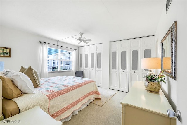 bedroom with a ceiling fan, visible vents, two closets, and light carpet