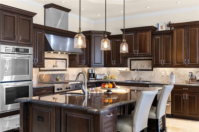 kitchen featuring double oven, a center island with sink, decorative light fixtures, dark stone counters, and wall chimney exhaust hood