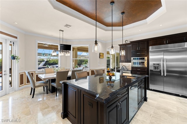 kitchen with pendant lighting, stainless steel appliances, a tray ceiling, and an island with sink