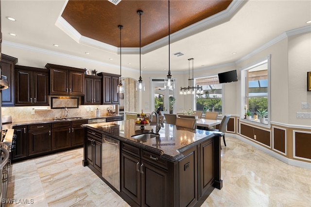 kitchen featuring sink, decorative light fixtures, a center island with sink, a tray ceiling, and dark stone counters