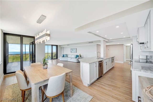 kitchen featuring pendant lighting, white cabinetry, sink, stainless steel dishwasher, and light stone counters