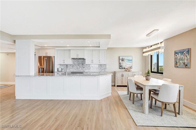 kitchen featuring stainless steel refrigerator with ice dispenser, hanging light fixtures, light stone countertops, decorative backsplash, and white cabinets