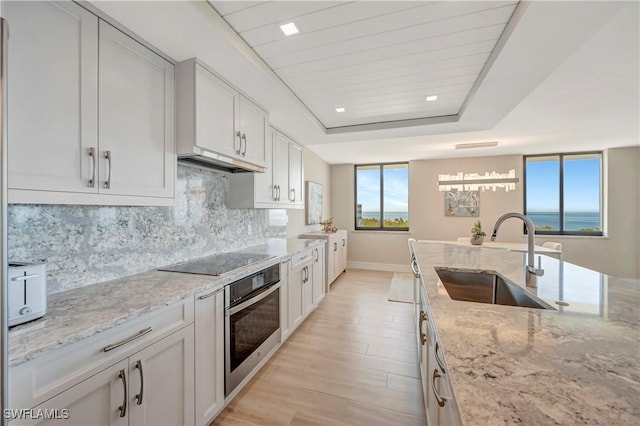 kitchen featuring light stone counters, black electric stovetop, oven, and sink