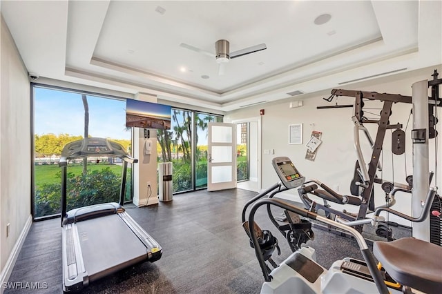 exercise room with floor to ceiling windows, ceiling fan, and a tray ceiling