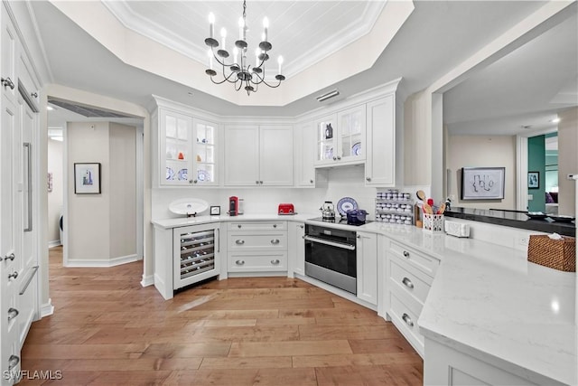 kitchen with oven, white cabinetry, pendant lighting, wine cooler, and a tray ceiling