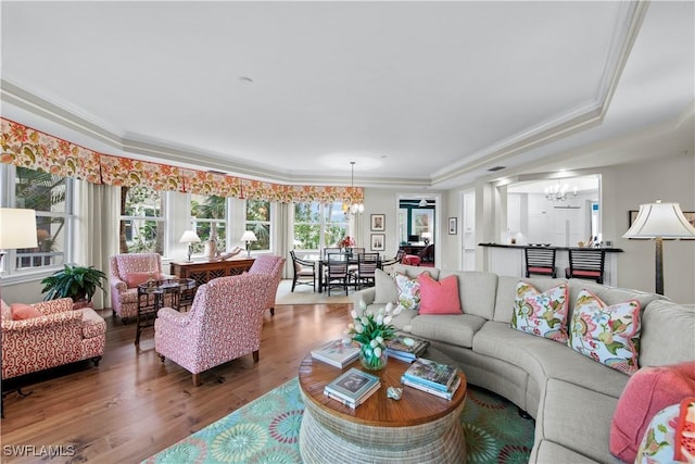 living room with a notable chandelier, hardwood / wood-style flooring, a raised ceiling, and crown molding