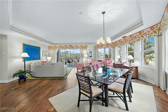 dining room featuring wood-type flooring, a notable chandelier, a tray ceiling, and ornamental molding